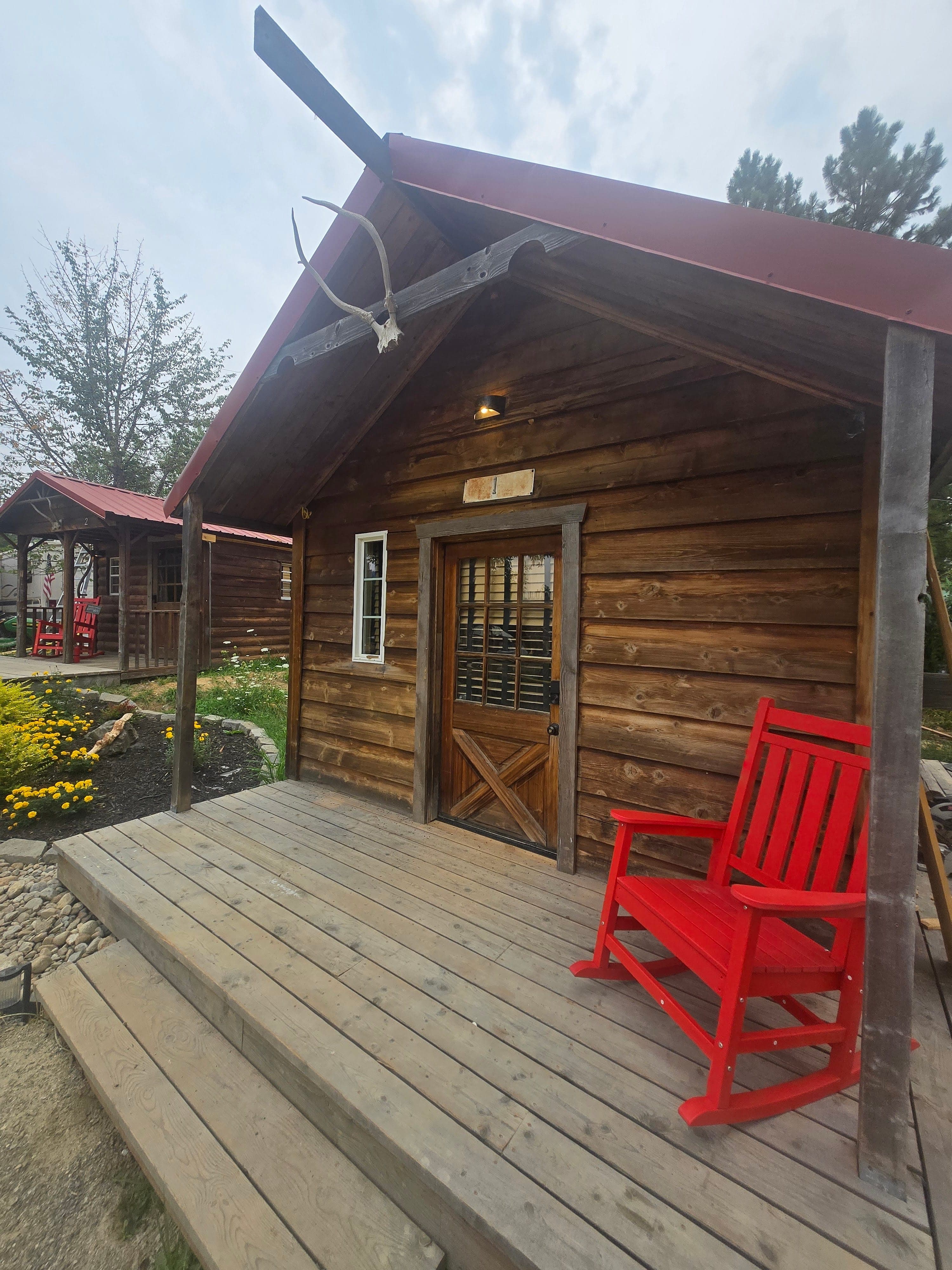 Log cabin porch with a single red rocker, antler cross above the door, and a marquee "1" sign