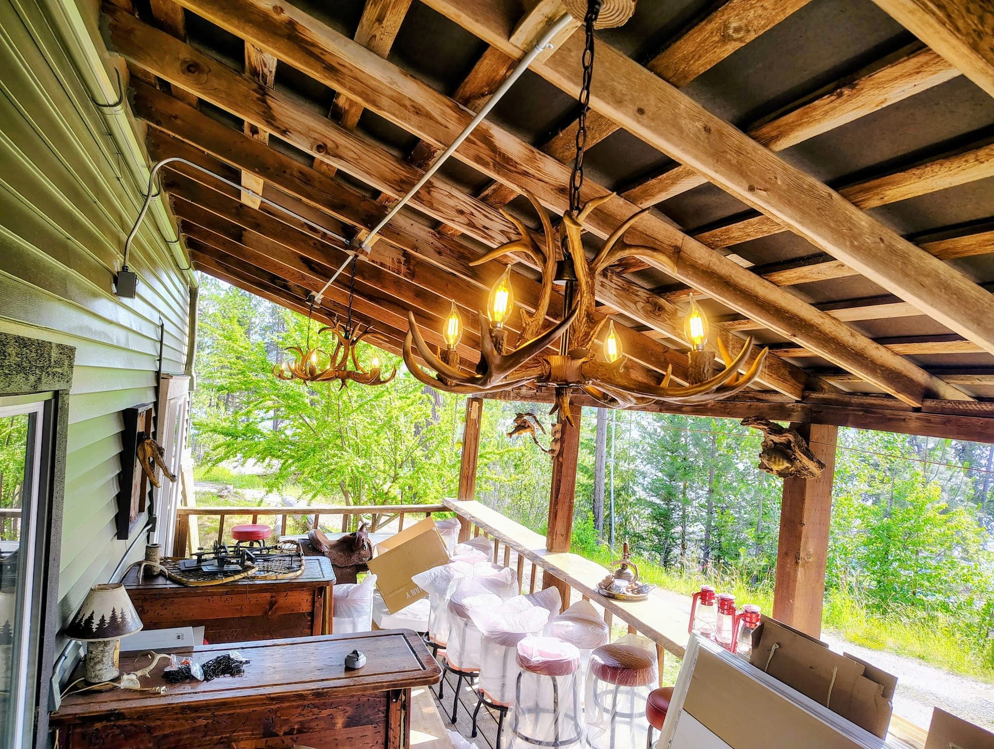 Covered lakefront deck at Red's Tavern with antler chandelier, bar setup, and forest views