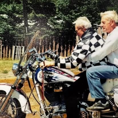 Vintage photograph of a couple riding a Harley-Davidson motorcycle past the Watson's property fence