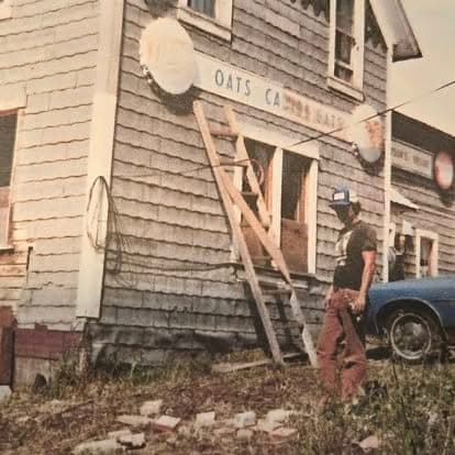 Vintage color photograph of the original 'Oats Cabins' on the Watson's property with a worker on a ladder repairing the exterior